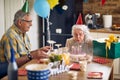 Happy senior woman blowing candles on her birthday cake, sitting at table with husband cheering her Royalty Free Stock Photo