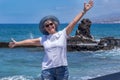 Happy senior woman with blue hat standing in front to the sea with open arms enjoying freedom and vacations Royalty Free Stock Photo