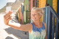 Happy senior woman clicking selfie while standing against beach hut Royalty Free Stock Photo