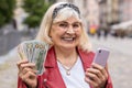 Happy senior woman counting money dollar cash, use smartphone calculator app in urban city street Royalty Free Stock Photo