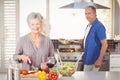 Happy senior woman cutting vegetables with husband in background Royalty Free Stock Photo