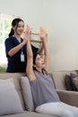 Happy senior woman doing exercise at home with asian female physiotherapist. Old retired lady doing stretching arms at