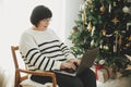 Happy senior woman in eyeglasses working on laptop in stylish festive christmas living room. Beautiful mature woman freelancer