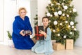 Happy senior woman giving christmas surprise to little girl at home. Excited granddaughter unpacking present under Royalty Free Stock Photo