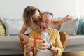 Happy senior woman giving gift box to her husband, congratulating with birthday, sitting on sofa at home Royalty Free Stock Photo