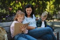 Happy senior woman with grandchildren sitting on bench and helping with homework outdoors in park. Royalty Free Stock Photo