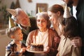 Happy senior woman holding cake with burning candles while celebrating birthday with big lovely family Royalty Free Stock Photo