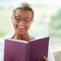 Happy senior woman, home and book with reading, sofa and relax in living room with story, knowledge and glasses. Elderly Royalty Free Stock Photo