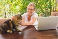 Happy senior woman with home cat use wireless headphones working online with laptop computer outdoor Royalty Free Stock Photo