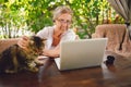 Happy senior woman with home cat use wireless headphones working online with laptop computer outdoor Royalty Free Stock Photo