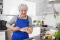 Happy senior woman in the kitchen preparing fresh fish. Royalty Free Stock Photo