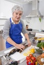 Happy senior woman in the kitchen preparing fresh fish.