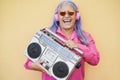 Happy senior woman listening music while holding boombox vintage stereo - Focus on face