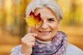 Happy senior woman with maple leaf at autumn park