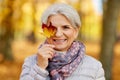 Happy senior woman with maple leaf at autumn park