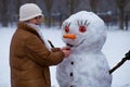 Happy senior woman sculpt and hug a big real snowman in winter Royalty Free Stock Photo