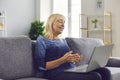 Happy senior woman sitting on couch at home and talking to family using video call app on laptop Royalty Free Stock Photo