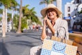 Happy senior woman sitting outdoor on a yellow bench using phone, attractive lady with hat and eyeglasses talking on mobile phone Royalty Free Stock Photo