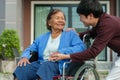 Happy senior woman sitting in wheelchair holding hand with young man grandson at outside house Royalty Free Stock Photo
