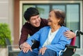 Happy senior woman sitting in wheelchair talking with young man grandson at outside house Royalty Free Stock Photo