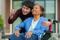 Happy senior woman sitting in wheelchair with young man grandson at outside house Royalty Free Stock Photo