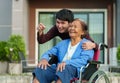 Happy senior woman sitting in wheelchair with young man grandson at outside house Royalty Free Stock Photo