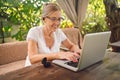 Happy senior woman use wireless headphones working online with laptop computer outdoor in garden Royalty Free Stock Photo