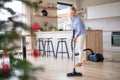 Senior woman with vacuum cleaner indoors at home at Christmas time, hoovering.