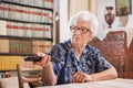 Happy senior woman watching tv and changing channel with remote control at home. Royalty Free Stock Photo