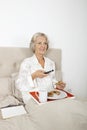 Happy senior woman watching TV while having breakfast in bed Royalty Free Stock Photo