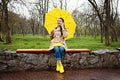 Happy senior woman in yellow rain coat with yellow umbrella is talking on a smartphone and walking in park. Staying in