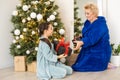 Happy senior woman giving christmas surprise to little girl at home. Excited granddaughter unpacking present under Royalty Free Stock Photo