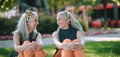 Happy seniors women, twins sitting in city park, smiling and talking.