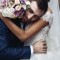 Happy sensual handsome groom hugging beautiful bride with bouquet in city streets closeup Royalty Free Stock Photo