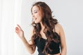 Happy sensual smiling girl asian young woman with dark long curly hair in black underwear looking at window with white curtain Royalty Free Stock Photo