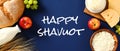 Happy Shavuot banner with dairy products, bread, fruits, wheat on blue background