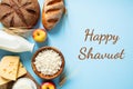 Happy Shavuot concept. Flat lay dairy products, cottage cheese, bottle of milk, wheat, cereal bread, cheese, apples on blue