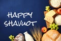 Happy Shavuot greeting card. Dairy food, wheat, grape, apples and cereal breads on blue background