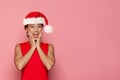 Happy shocked Christmas woman in Santa hat having fun on pink background