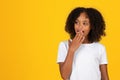 Happy shocked curly teen black girl in white t-shirt covers open mouth with hand, look at free space