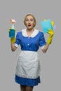 Happy shocked maid in uniform holding rags and detergent.