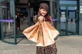 A happy shopaholic girl keeps her bags near the shopping center. A woman near the store is happy with her purchases