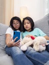 Happy siblings children sitting on sofa in living room speak with parent on mobile phone together, smiling elder girl showing cute