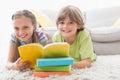 Happy siblings reding book while lying on rug