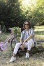 Happy similing teenager with long hair looking to camera enjoying his spare time with his new retro pink bike