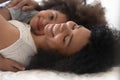 Happy single african american mommy lying on bed with daughter.