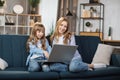 Happy sisters or friends two cute blond girls sitting together on comfortable couch, using laptop Royalty Free Stock Photo