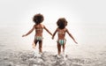 Happy sisters running inside water during summer time - Afro kids having fun playing on the beach Royalty Free Stock Photo