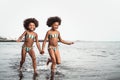 Happy sisters running inside water during summer time - Afro kids having fun playing on the beach