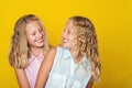 Happy sisters smiling and having fun together. Beauty and fashion. Cute twins girls on yellow background